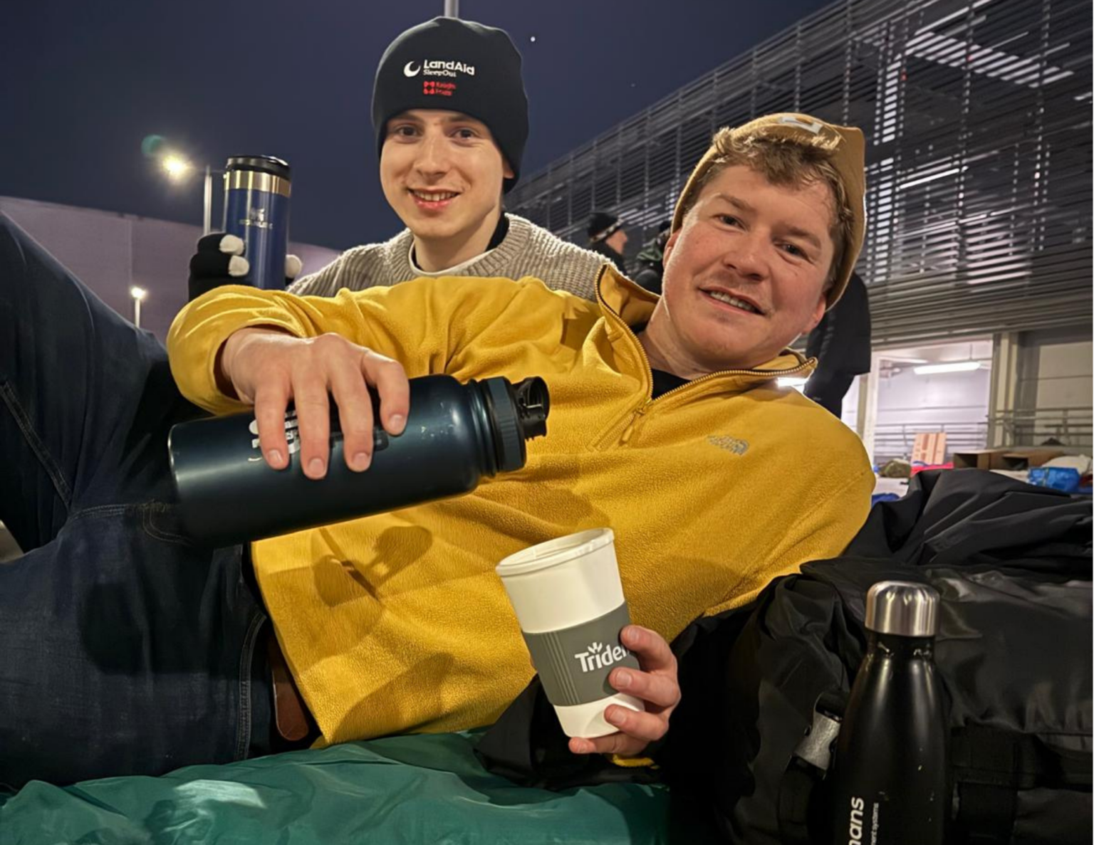 Two members of our team at the LandAid Sleepout. Callum is pouring coffee into a Trident mug.