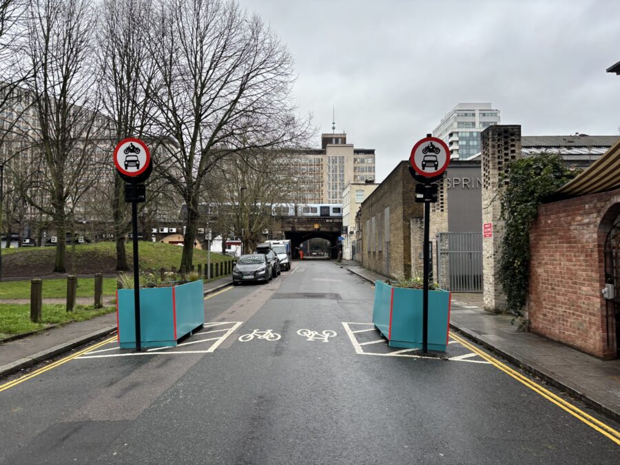 Image of a road with two road signs in the foreground and a train tunnel in the background. 