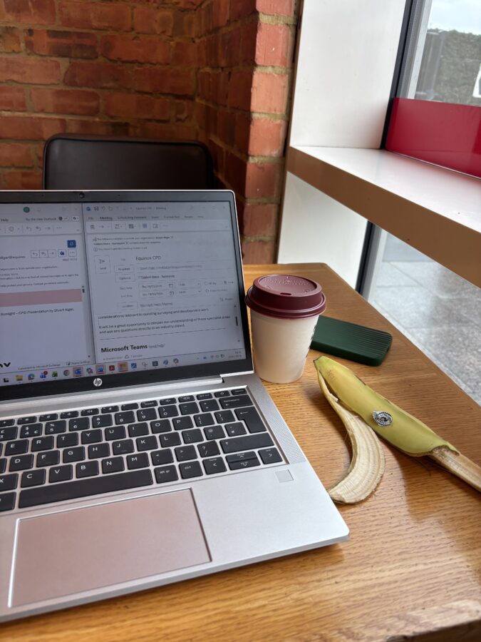 Image of a laptopn on a table in a coffee shop. Takeaway coffee cup and banana peel on the side. 