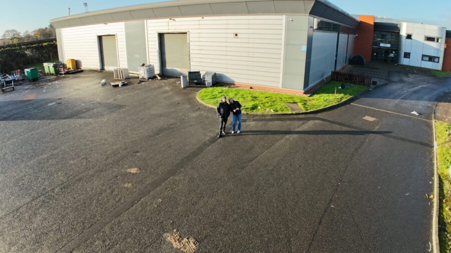 Image looking at an industrail building, with the two surveyors on the ground.